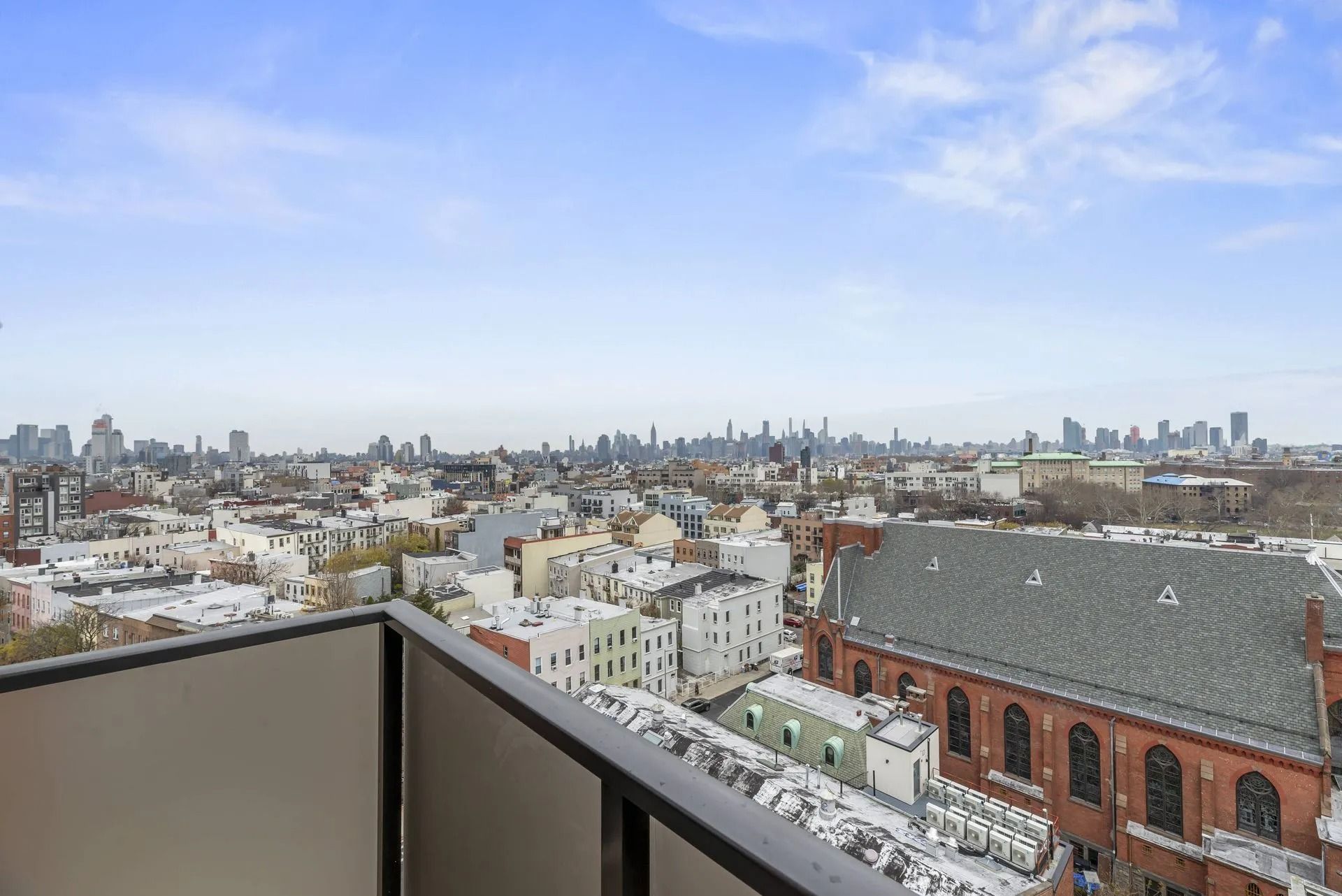 City skyline viewed from a balcony, with snowy rooftops and a red-brick building in the foreground.