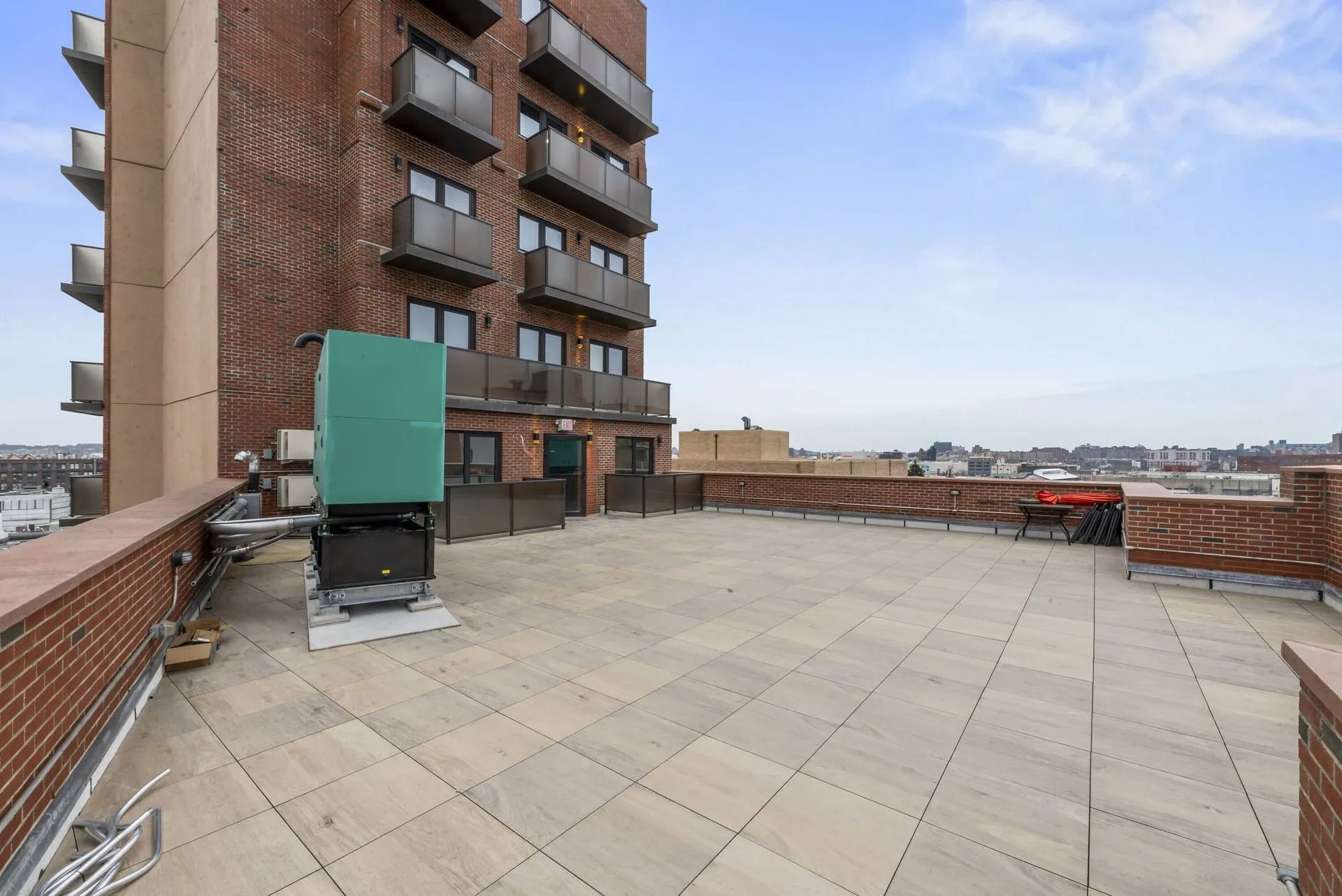 Rooftop terrace with tan pavers, brick walls, and an apartment building with balconies