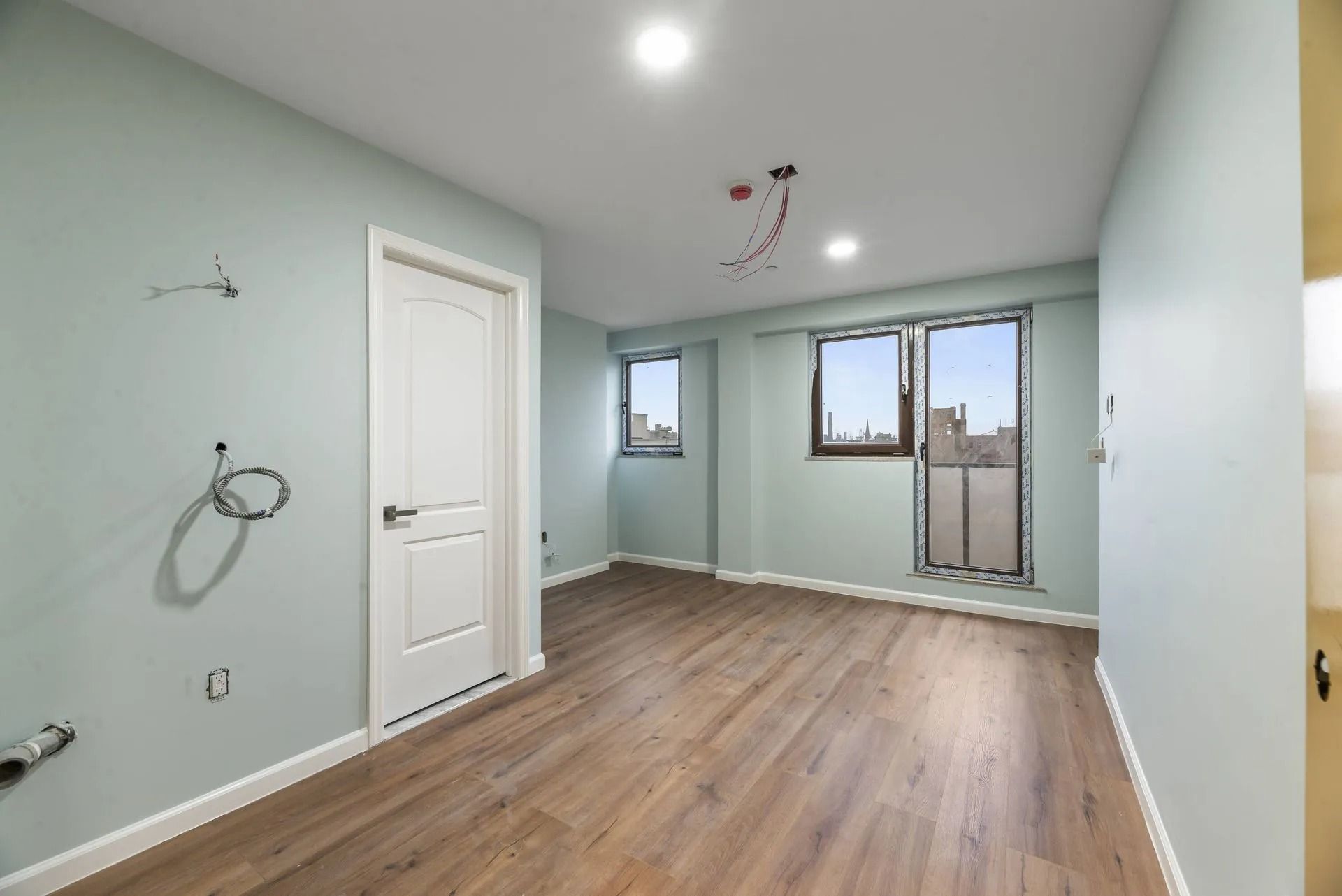Empty mint-green room with wood floors, recessed lights, and a glass door to a small balcony.
