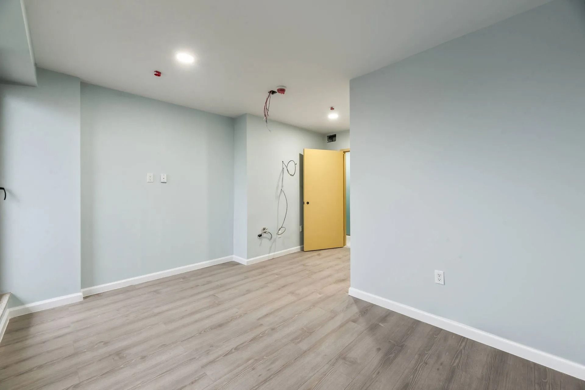 Empty modern room with light gray walls, wood-look flooring, and a yellow door