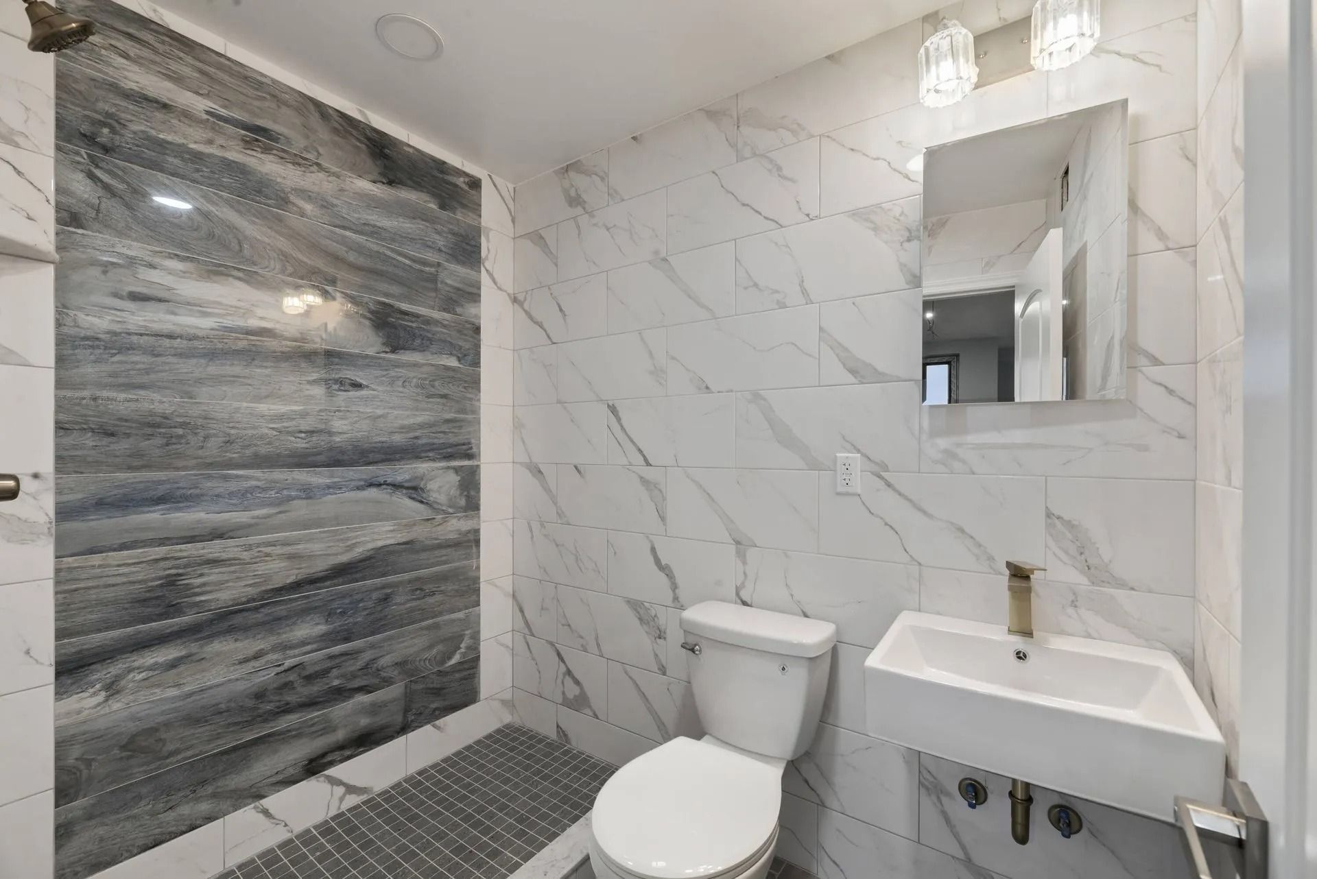 Modern bathroom with marble-look walls, a toilet, sink, mirror, and tiled shower area