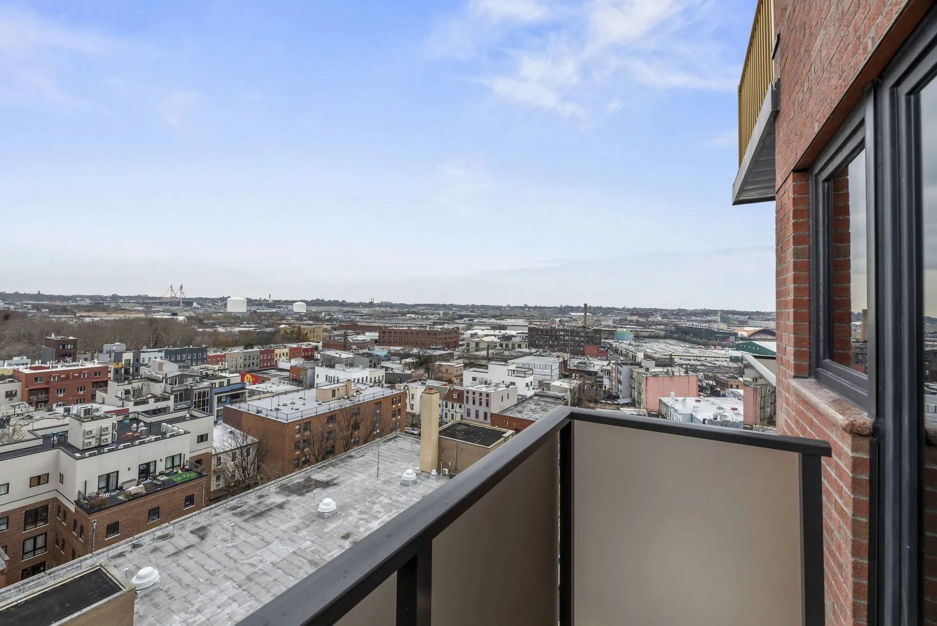 Balcony view of a snowy cityscape with rooftops and distant buildings under a cloudy sky