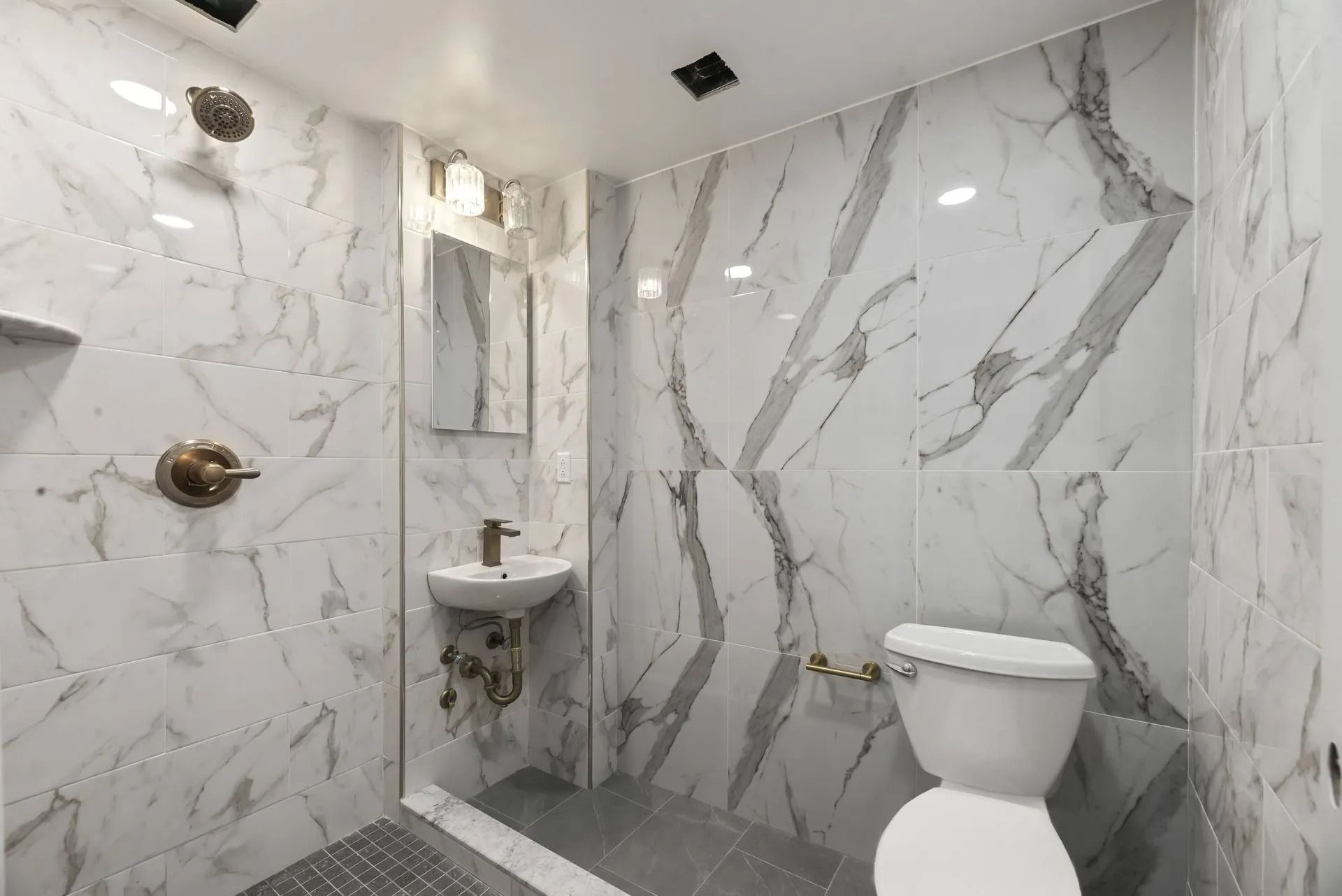 Modern marble bathroom with toilet, small sink, and shower fixtures