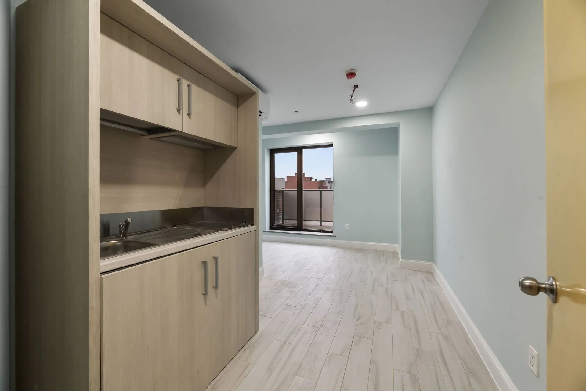 Empty modern room with light wood cabinetry and a large window at the far end.