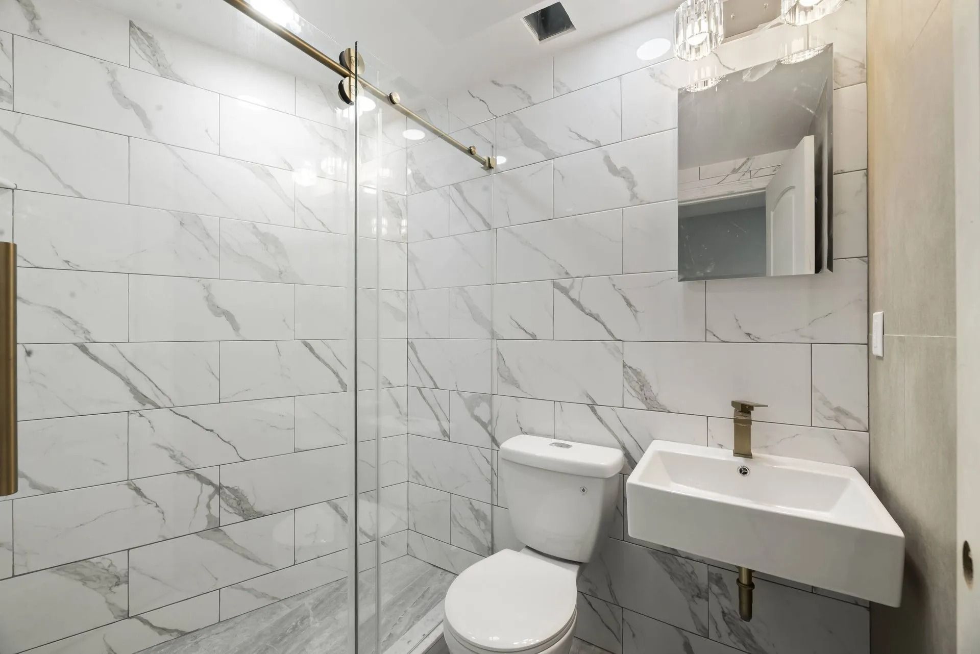 Small white-tiled bathroom with toilet, wall-mounted sink, shower, and mirror.