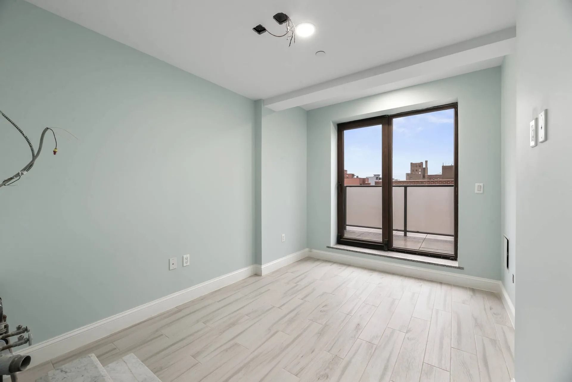 Empty light-gray room with white floors, balcony doors, and city view