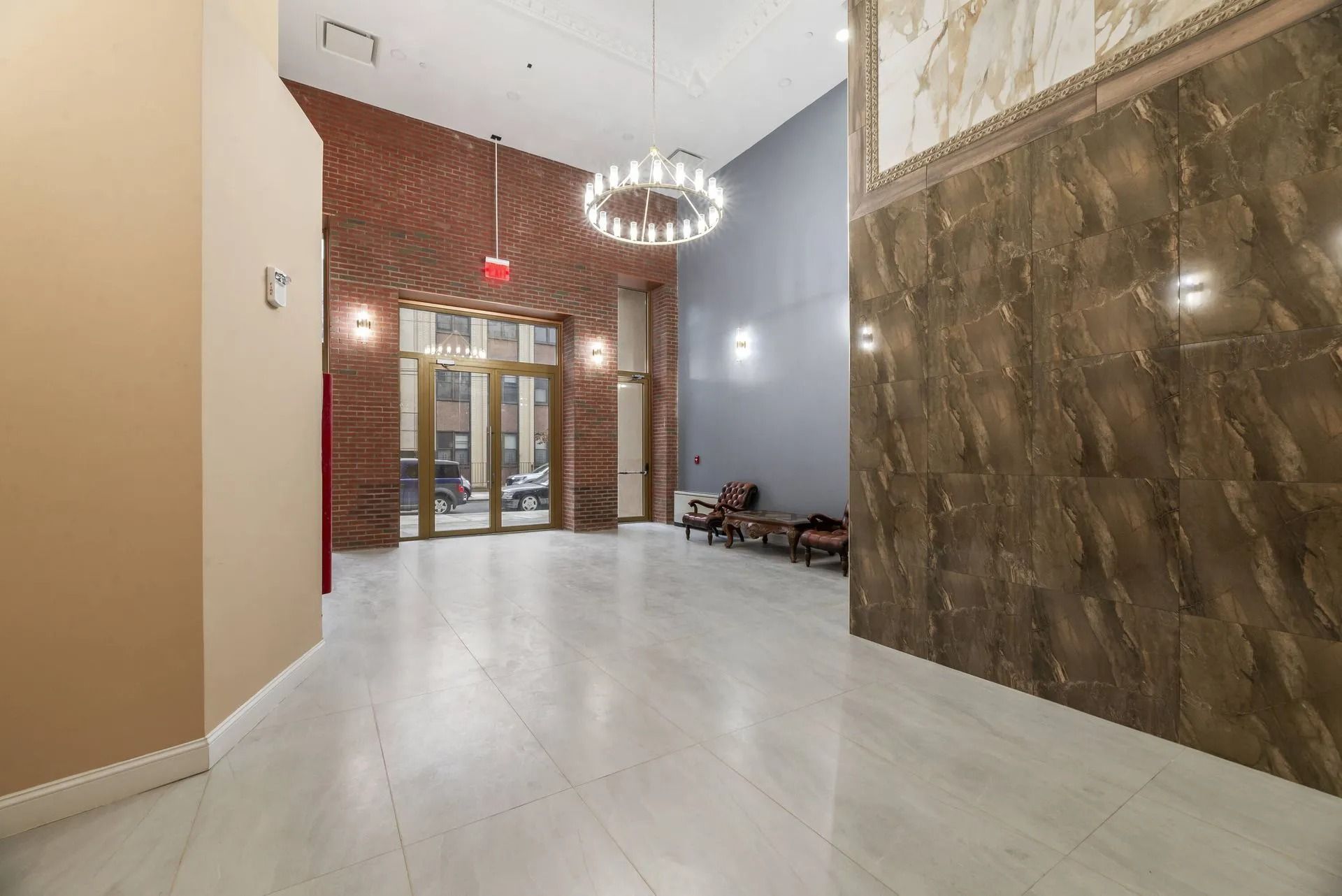 Modern lobby with marble floors, chandelier, red accent wall, and glass entrance doors