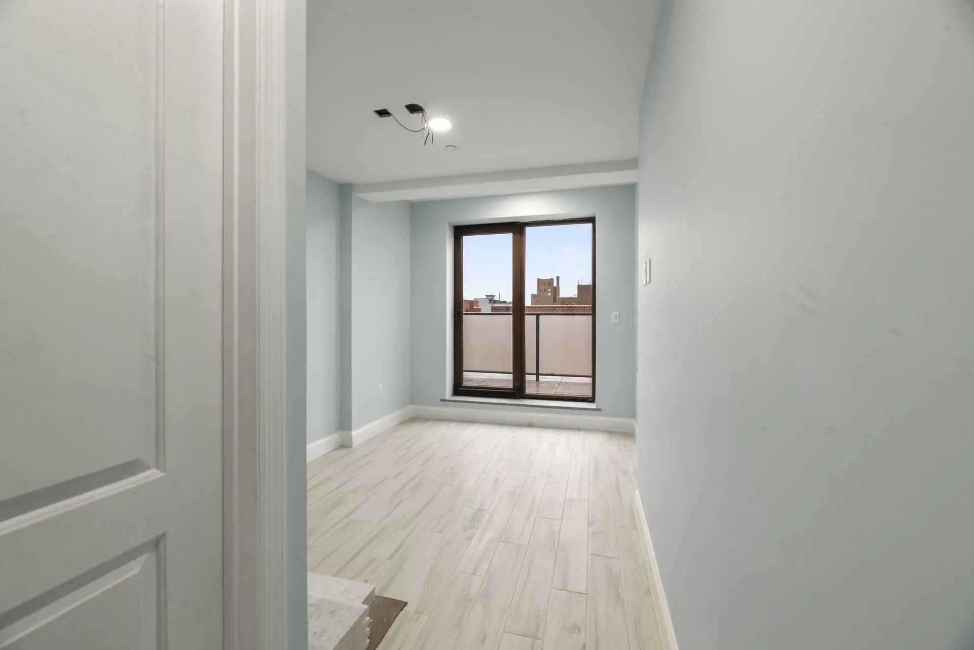 Empty white hallway leading to a bright room with a balcony door.