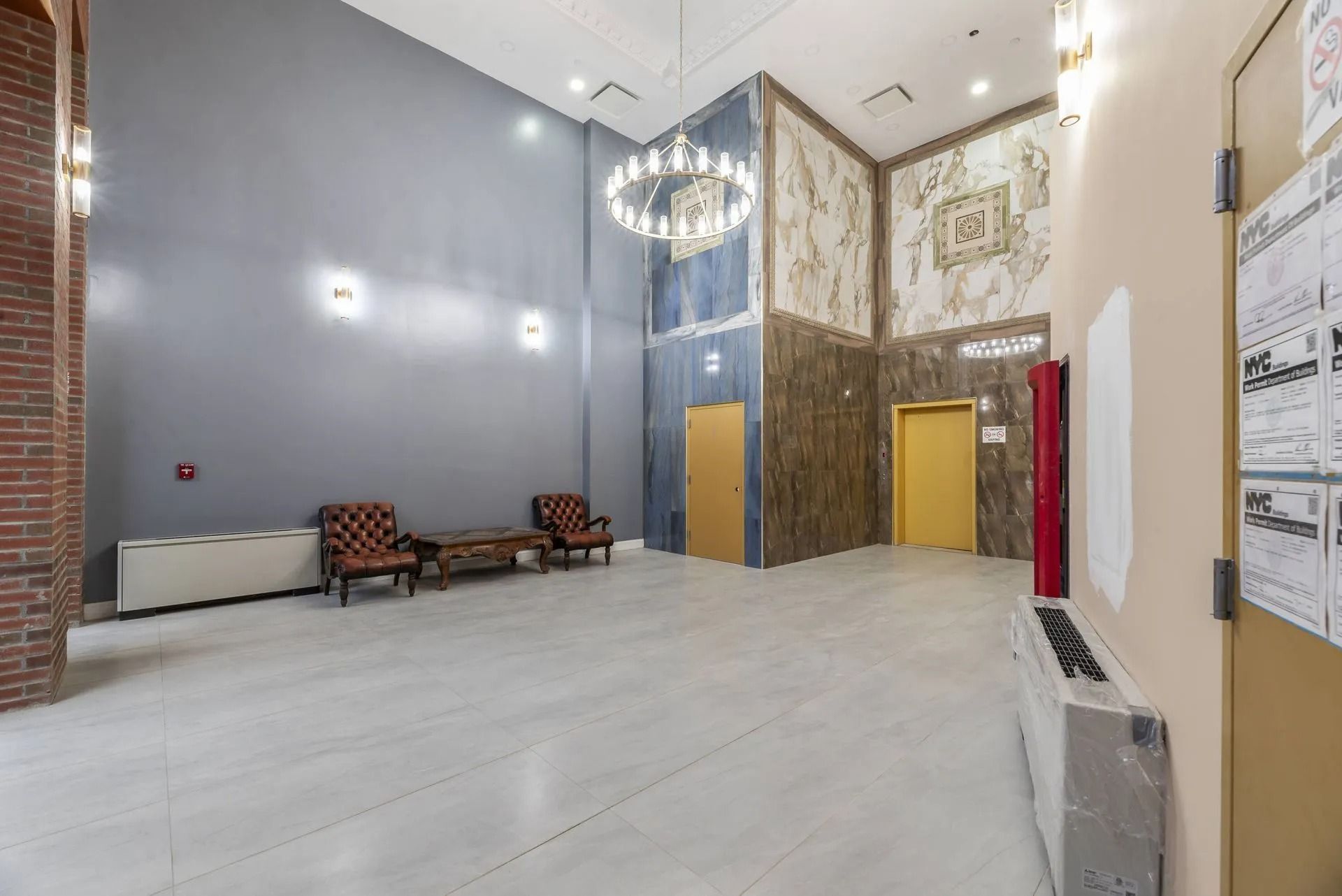 Spacious lobby with white floors, brick and gold walls, benches, and a chandelier under high ceilings
