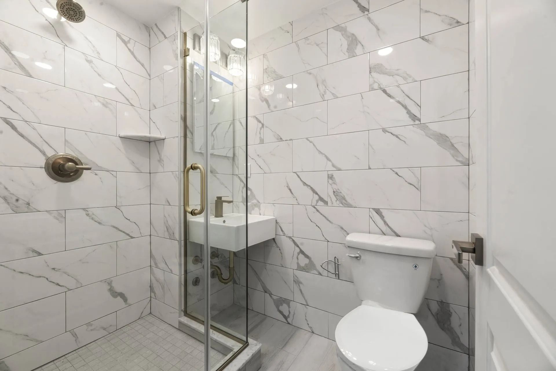 Modern white marble-tile bathroom with glass shower, vanity, and toilet