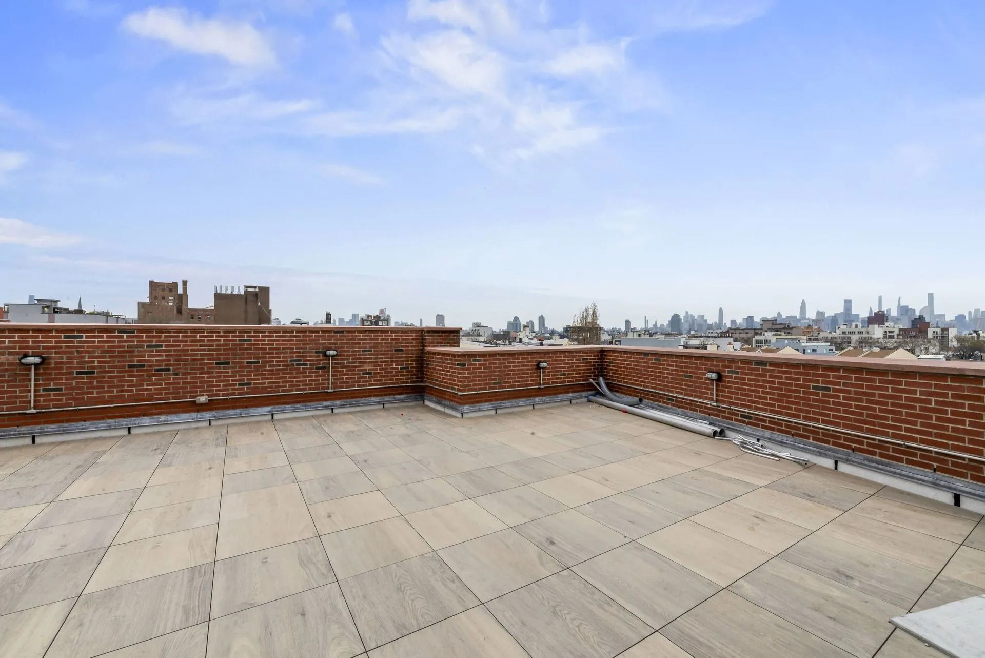 Empty rooftop terrace with brick parapet walls and a distant city skyline under a blue sky