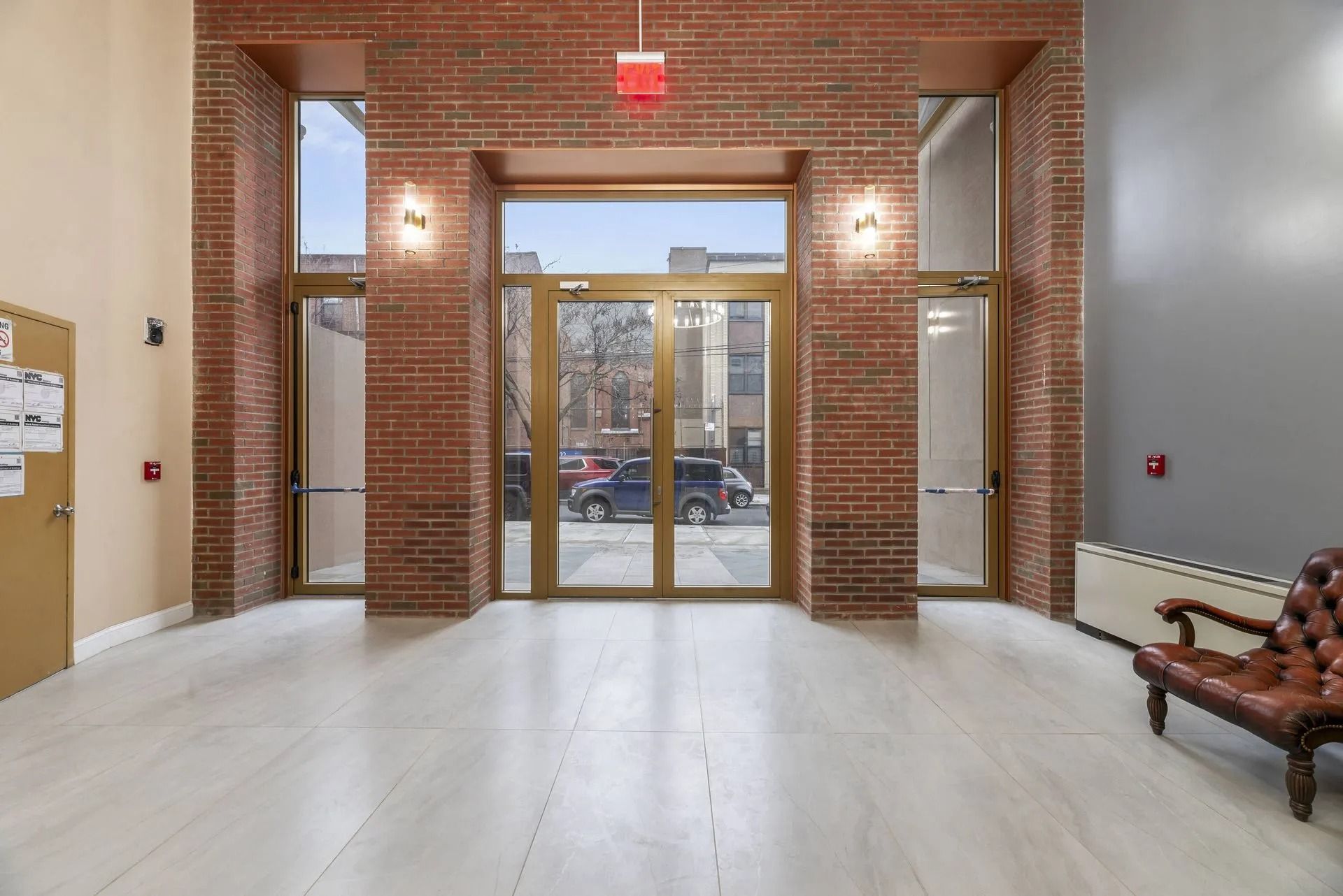 Empty brick lobby with glass double doors, white floor, and a wooden bench.