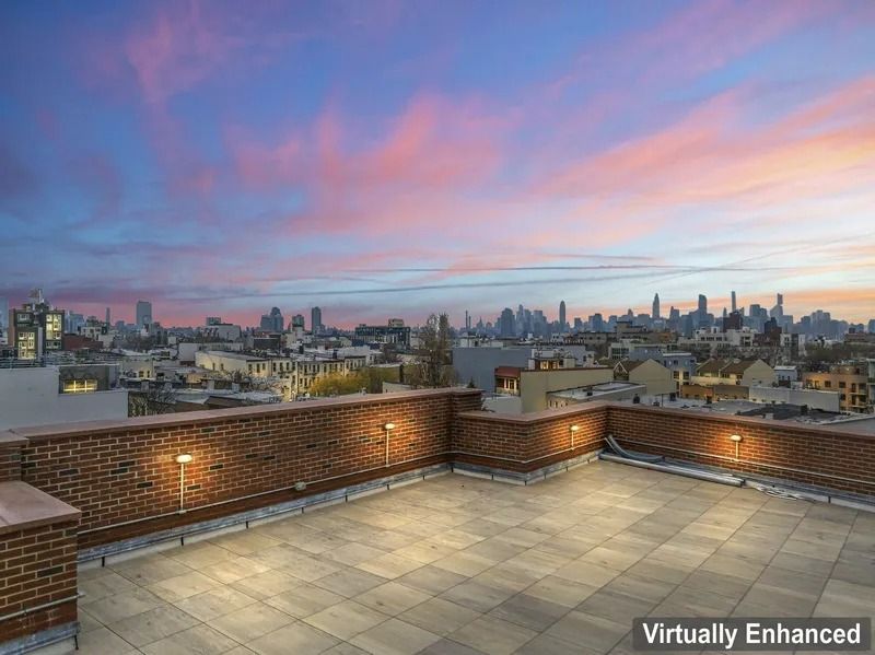 Rooftop terrace with brick walls overlooking a city skyline at sunset, pink and blue sky.