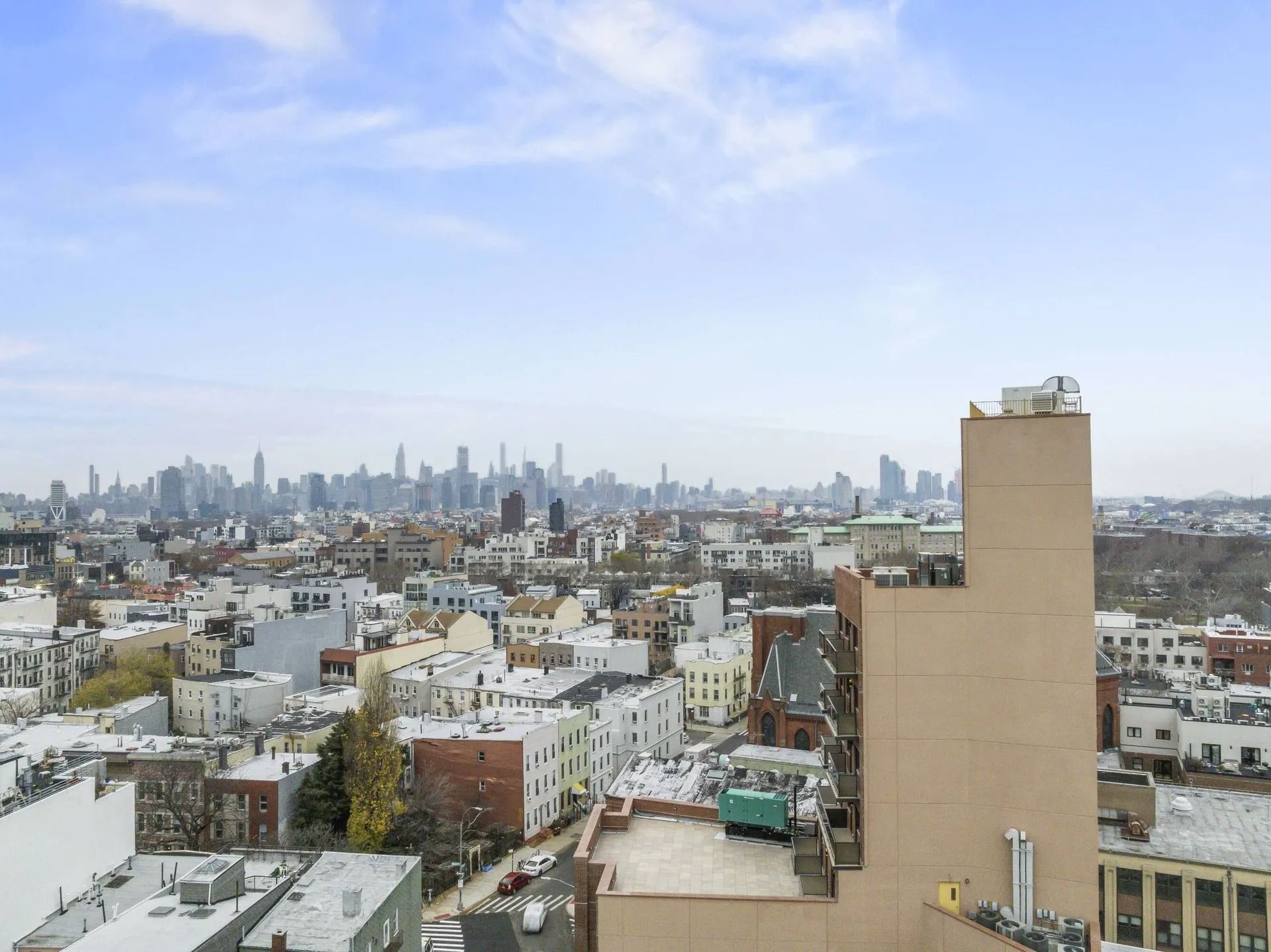 City skyline view from rooftops under a pale blue sky, with low-rise buildings in the foreground.