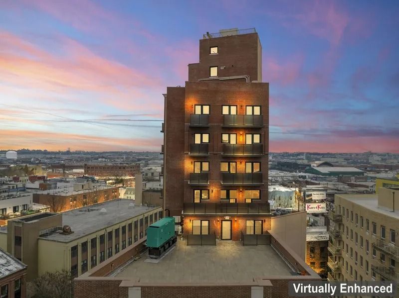 Tall brick building at dusk with glowing windows, overlooking a city under a pink-blue sky.