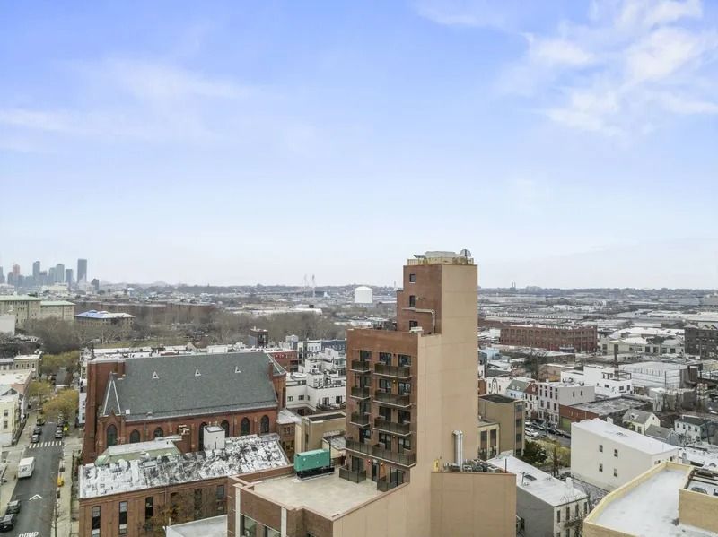 City skyline with a beige high-rise and low buildings under a cloudy blue sky