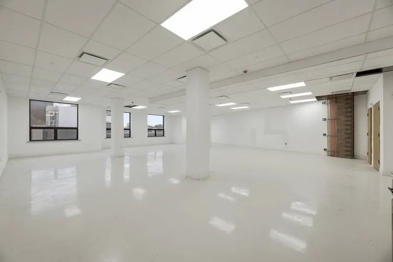 Empty white office space with glossy floor, ceiling lights, windows, and columns