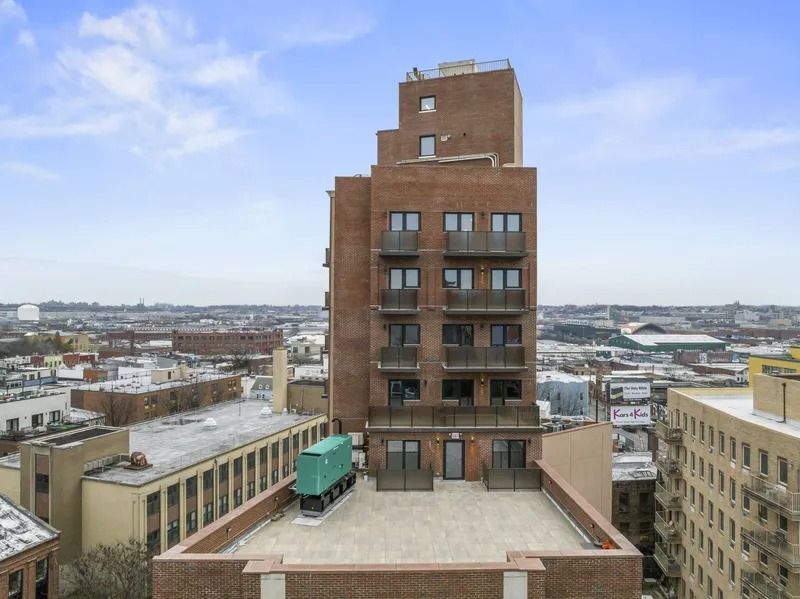Rooftop view of a tall brick building with snowy cityscape and a pale blue sky beyond.