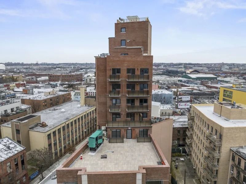 Snowy cityscape with a central brick building and surrounding rooftops under a cloudy sky