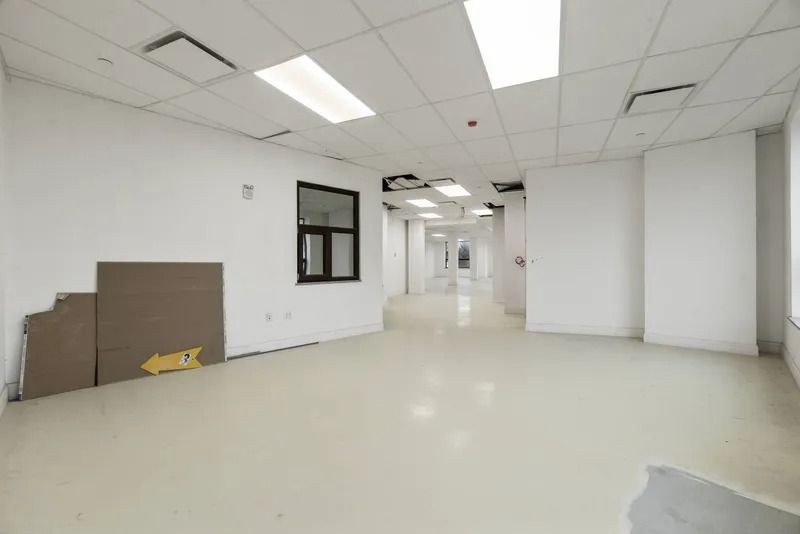 Empty white office space with beige floor, drop ceiling, and windows along the corridor