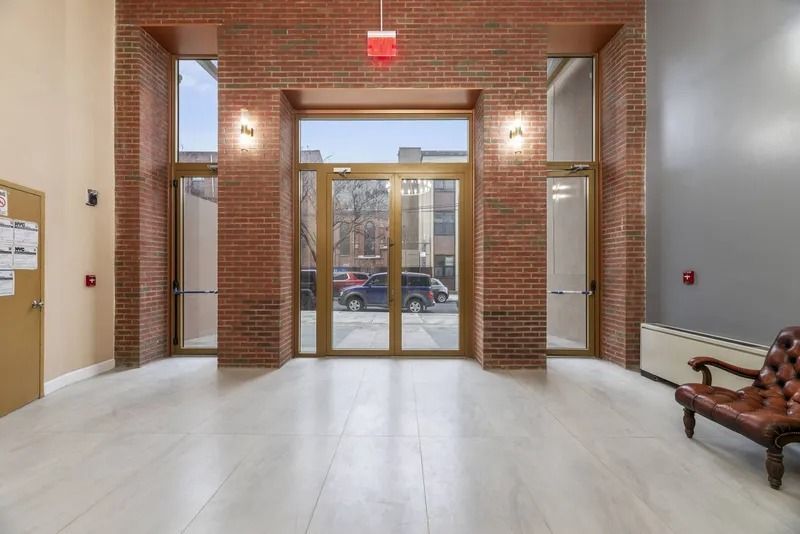 Empty brick-walled lobby with glass double doors and a bench on the right.