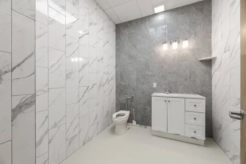 Modern bathroom with marble walls, gray accent wall, white vanity, toilet, and glass shower area