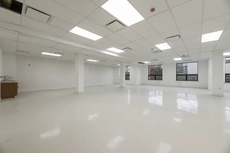 Bright empty office space with white floors, ceiling lights, and large windows