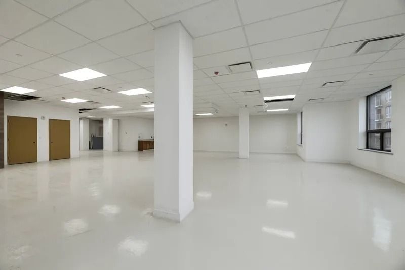Empty white office space with columns, fluorescent ceiling lights, doors, and windows