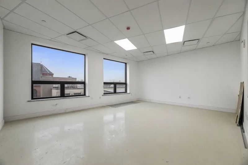 Empty white office room with large windows, tile floor, and drop ceiling lights