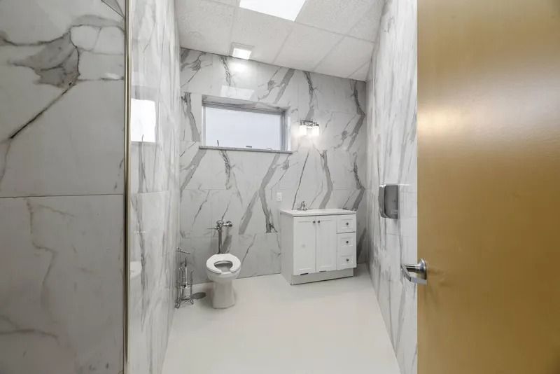 Modern bathroom with marble-look tiles, wall-mounted toilet, sink cabinet, and wooden door partly open