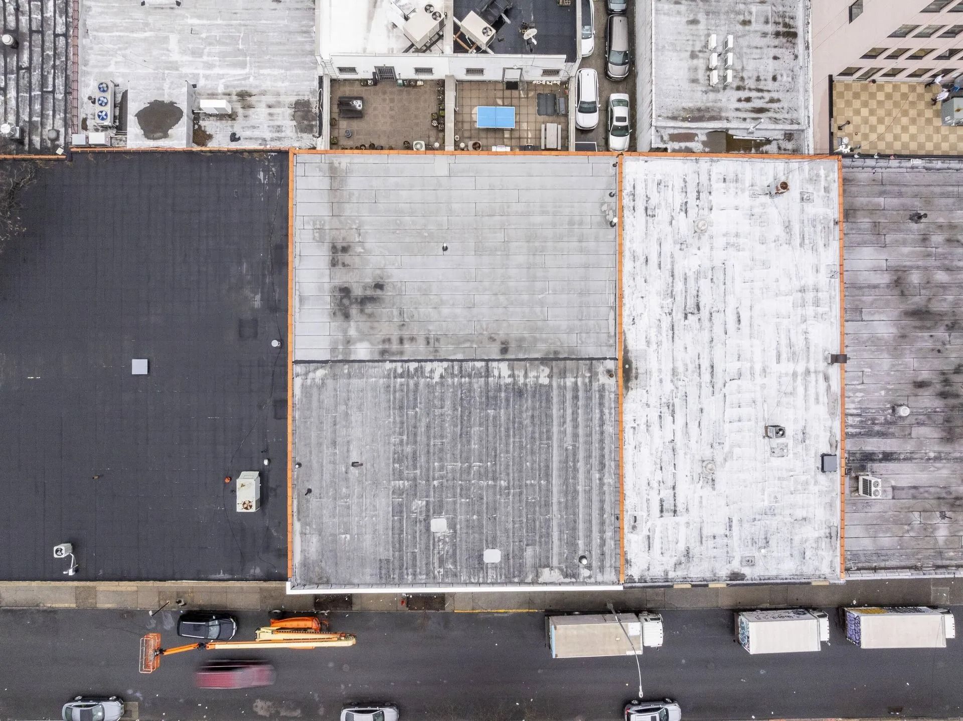 Aerial view of three flat-roofed buildings beside a street with parked vehicles.