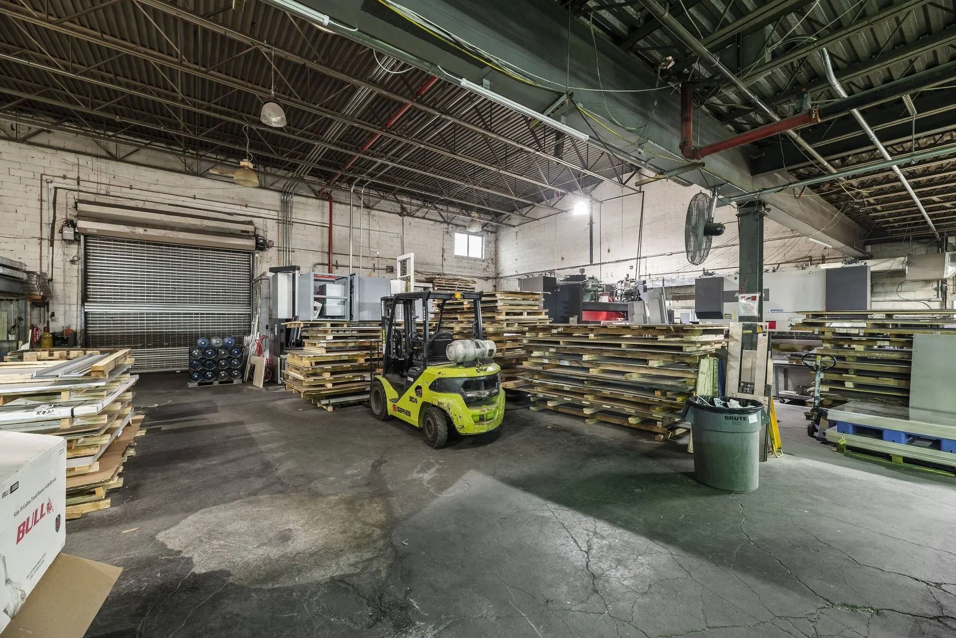 Warehouse interior with stacked pallets, a yellow forklift, and industrial shelving under a high ceiling