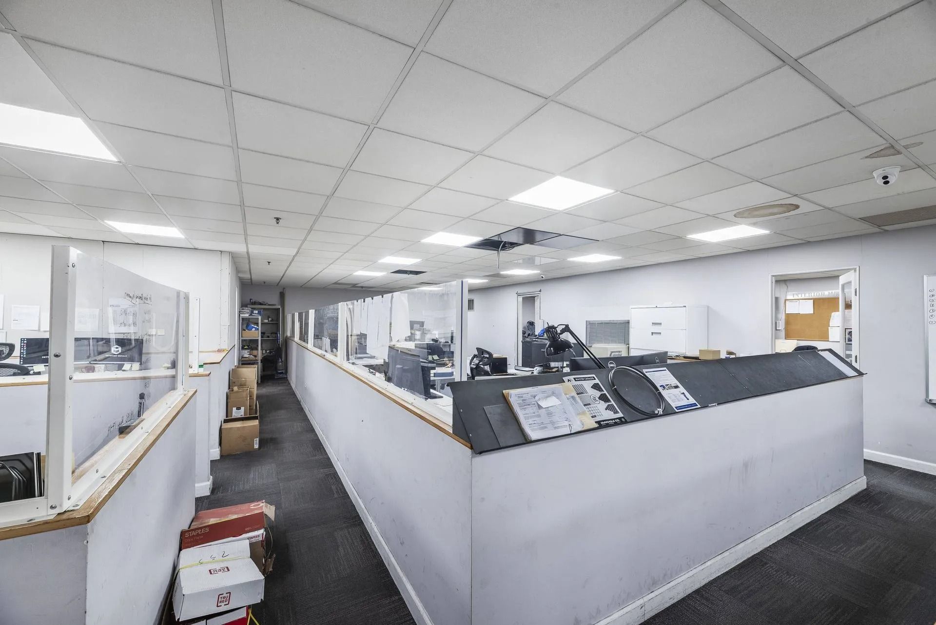 Office interior with desks, monitors, and a large central counter under fluorescent lighting