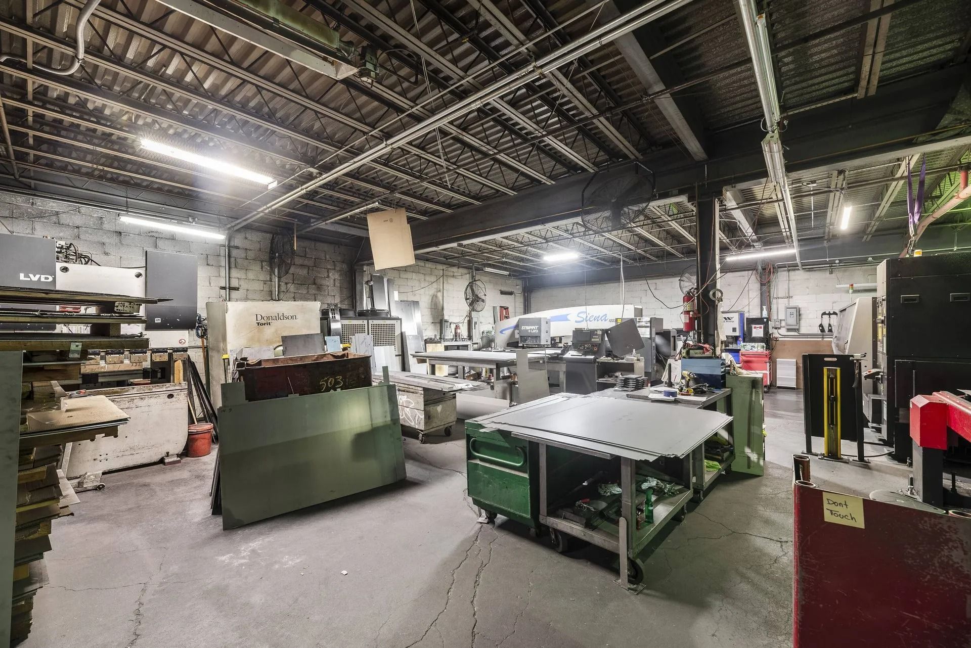Industrial workshop with machinery, worktables, and shelves under a high metal ceiling