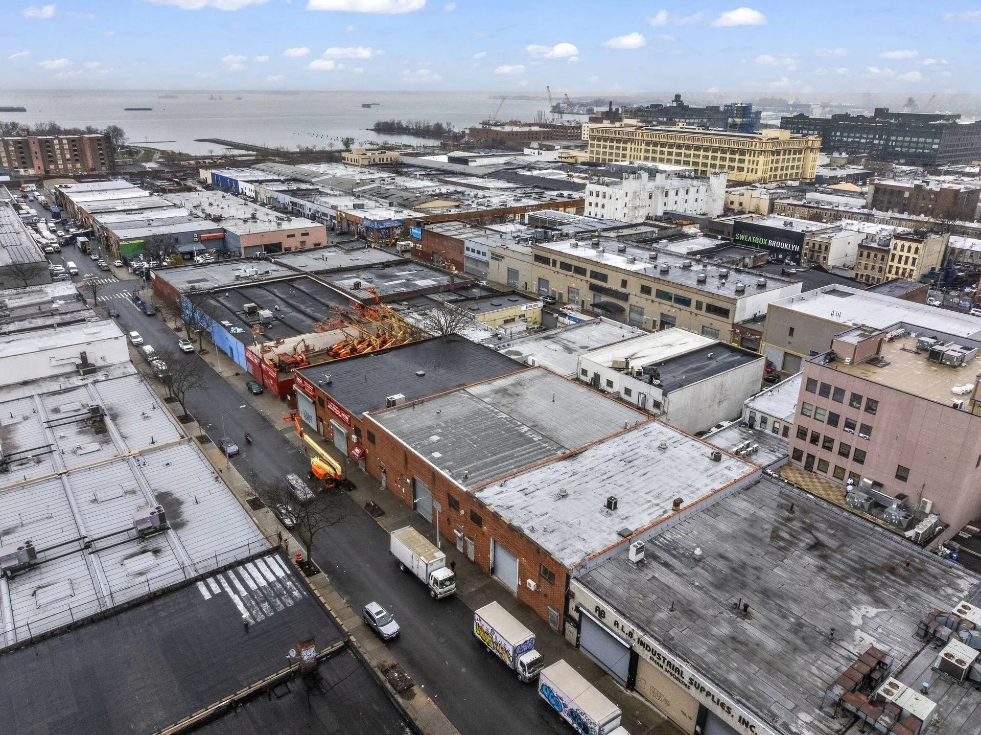 Aerial view of a snowy industrial neighborhood with warehouses, trucks, and streets under a cloudy sky