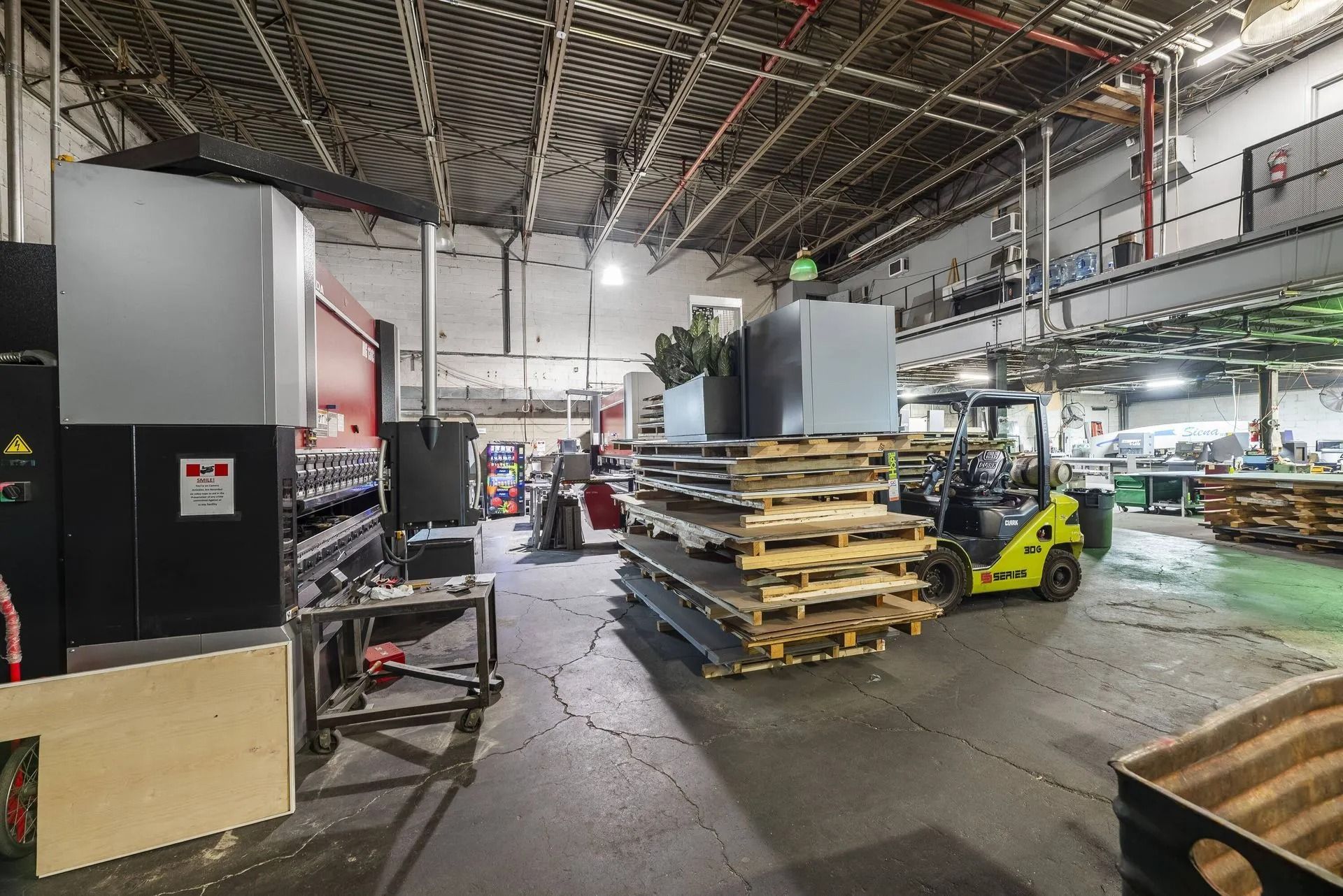 Industrial warehouse with stacked pallets, machinery, and a yellow forklift under a high ceiling