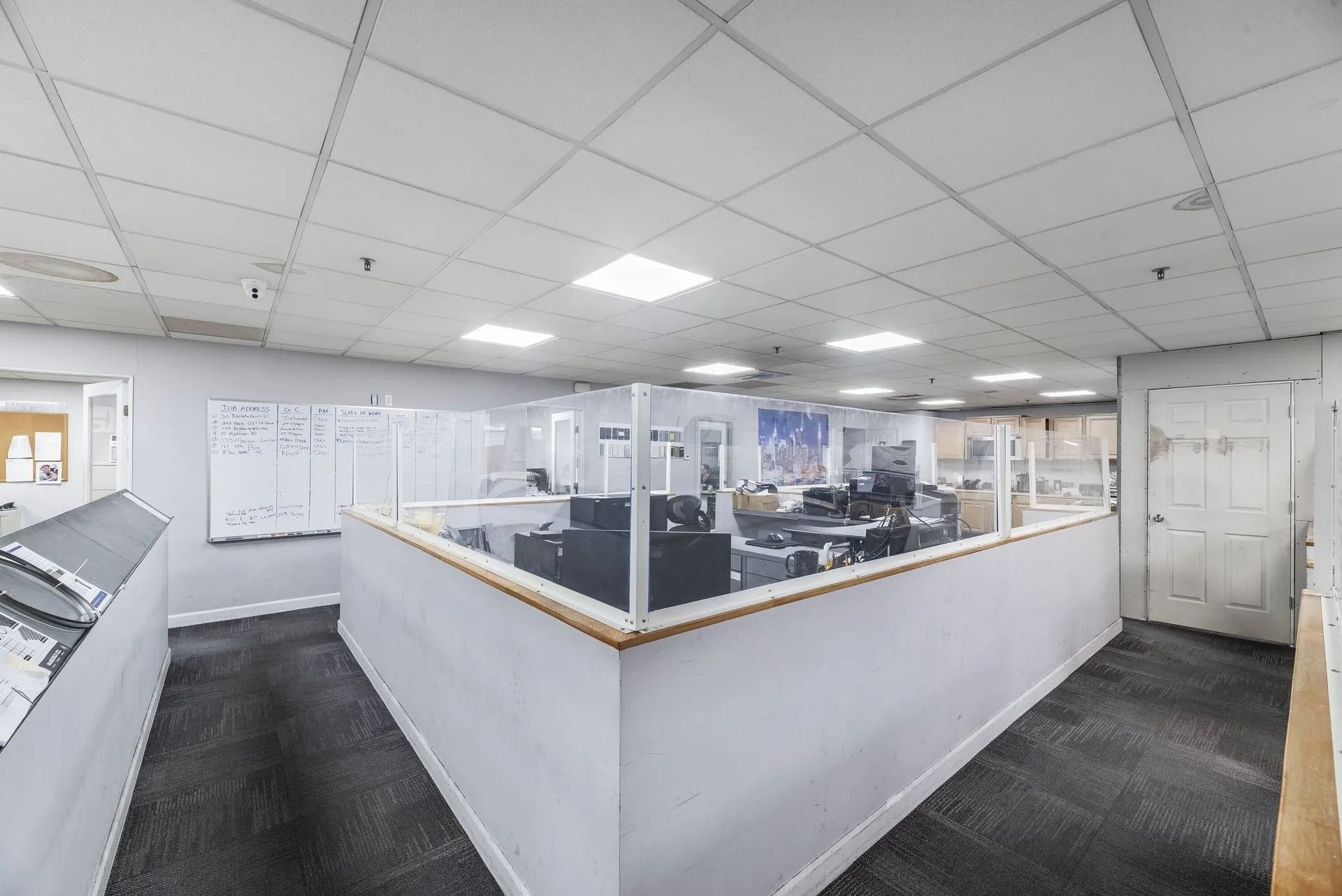 Modern office cubicle area with desks, computers, and fluorescent ceiling lights