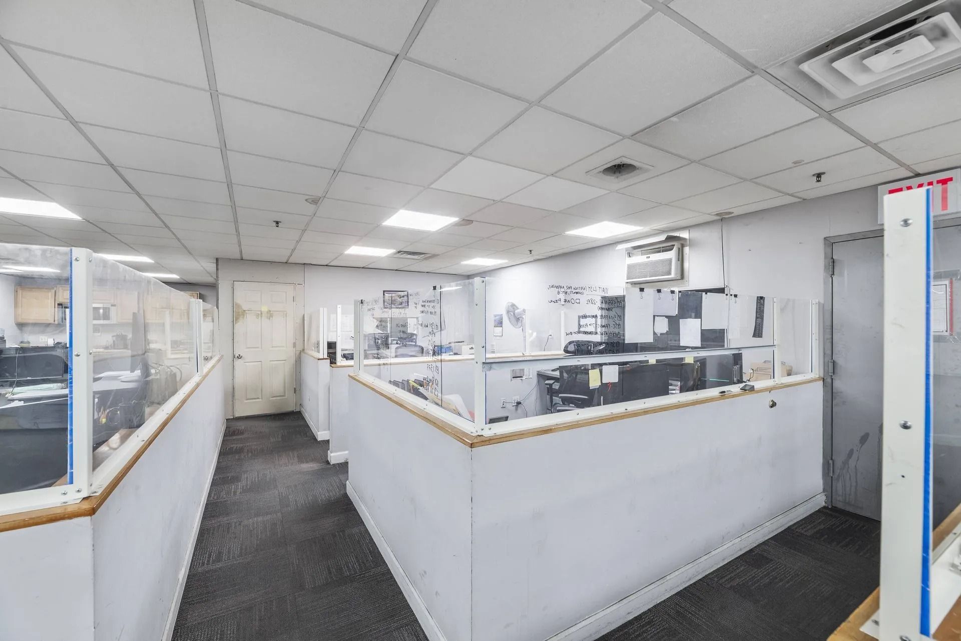 Open office cubicles with computer desks and white walls under fluorescent ceiling lights