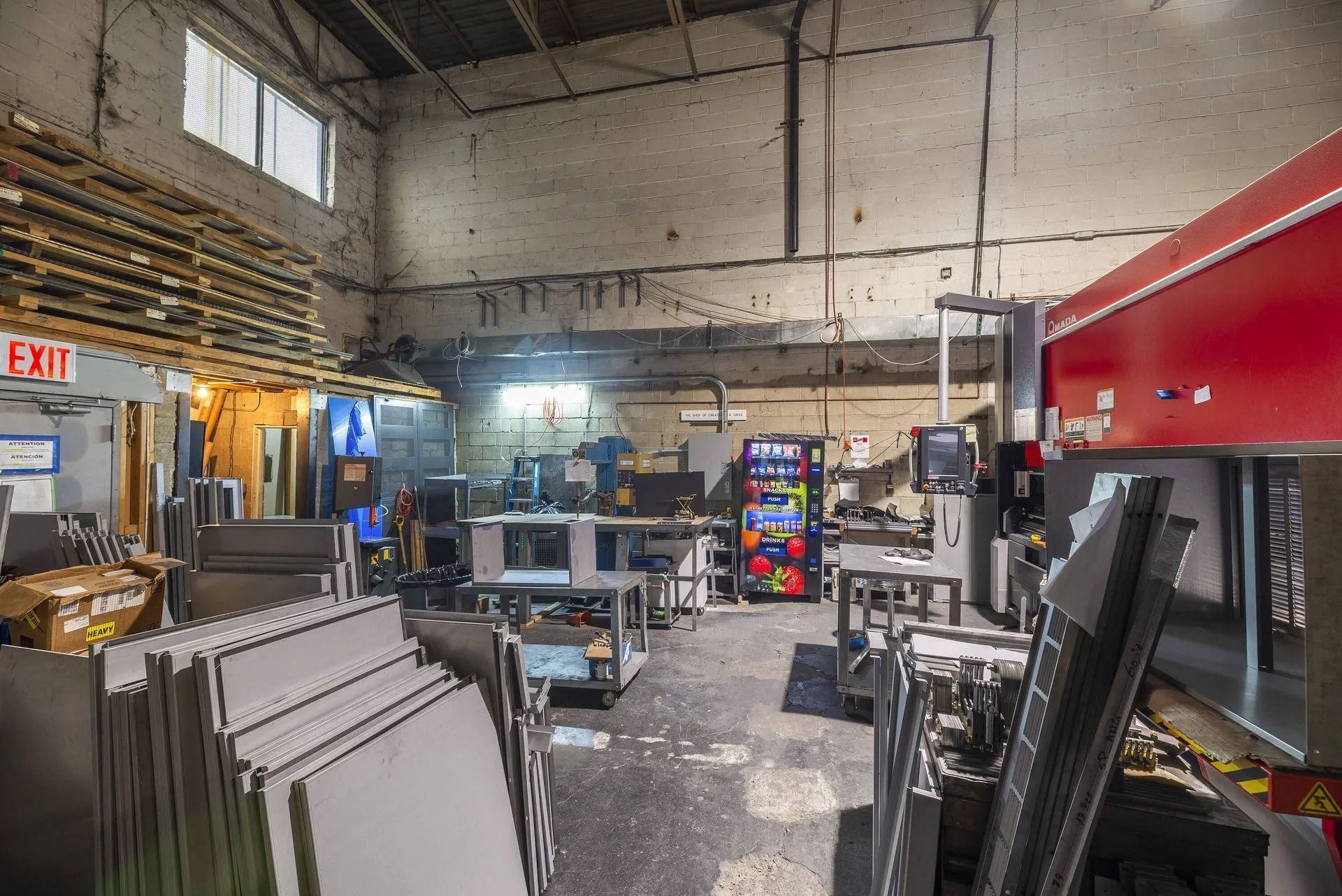 Industrial workshop with stacked materials, equipment, and a large red machine inside a warehouse.