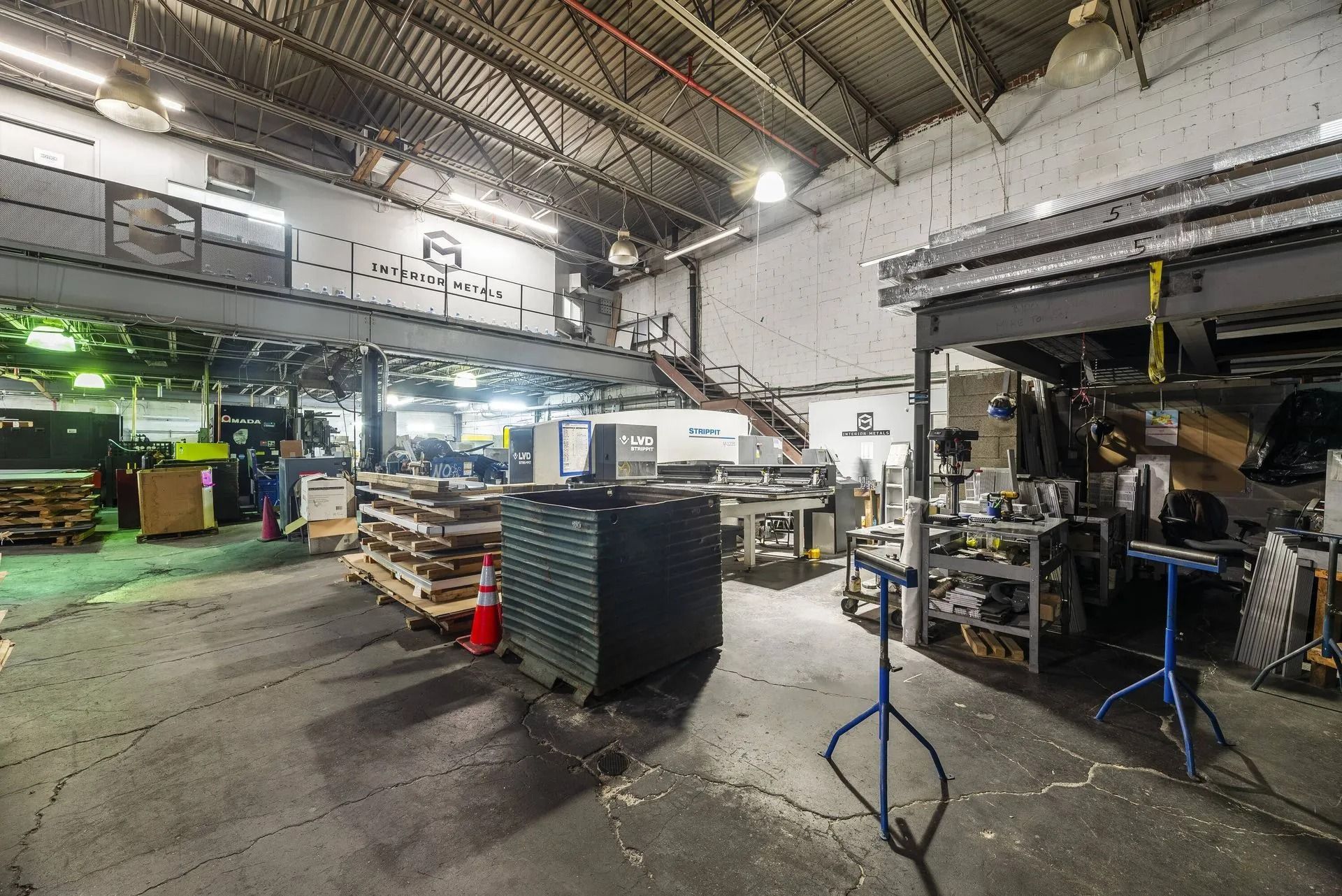Industrial workshop interior with machinery, metal shelves, and a concrete floor under bright overhead lights