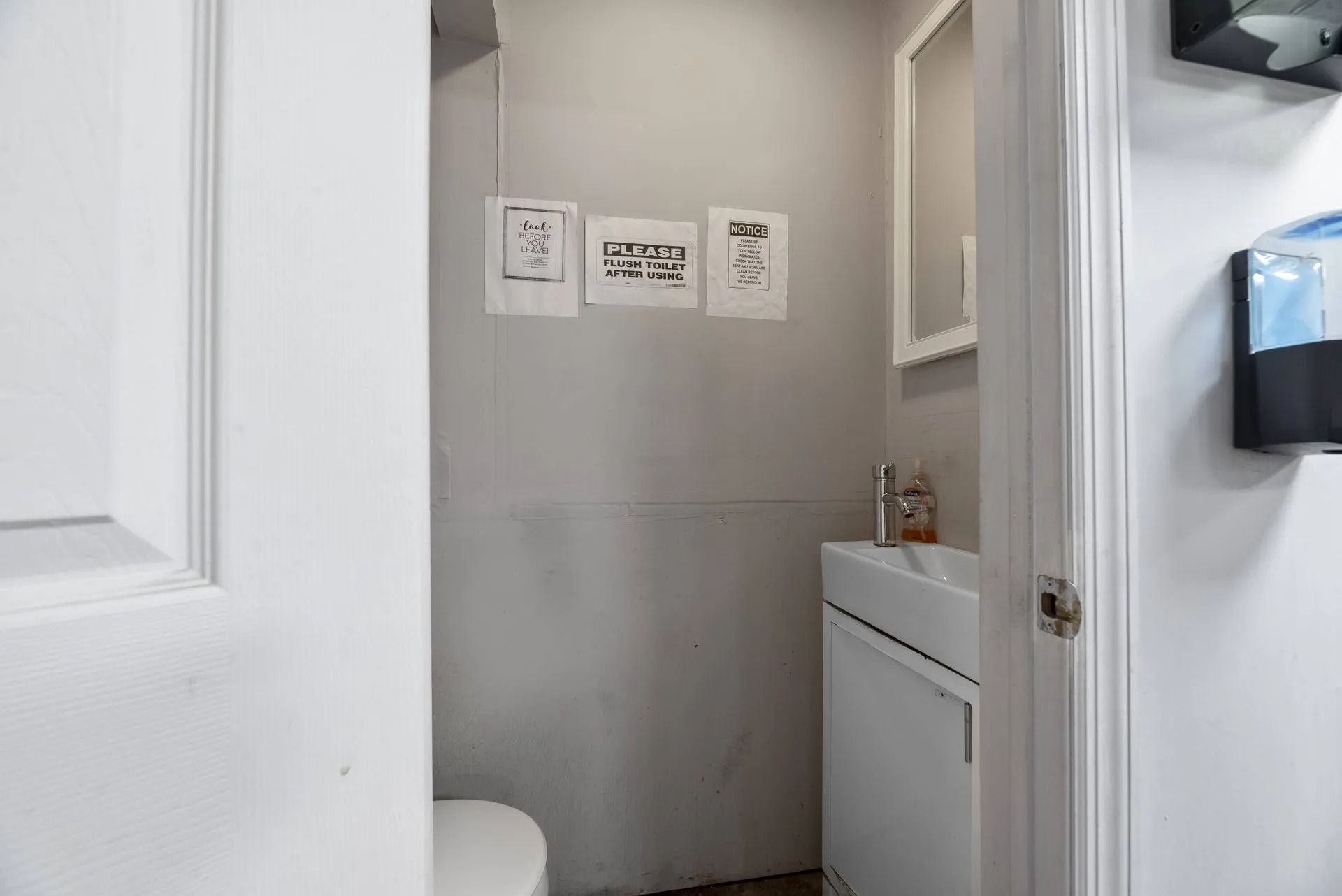 Small bathroom with white door, toilet, sink, and wall signs in a narrow alcove.