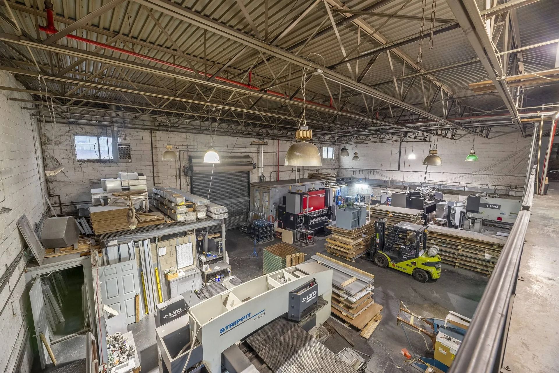 Wide-angle view of a factory workshop with machinery, stacks of materials, and exposed metal ceiling beams.