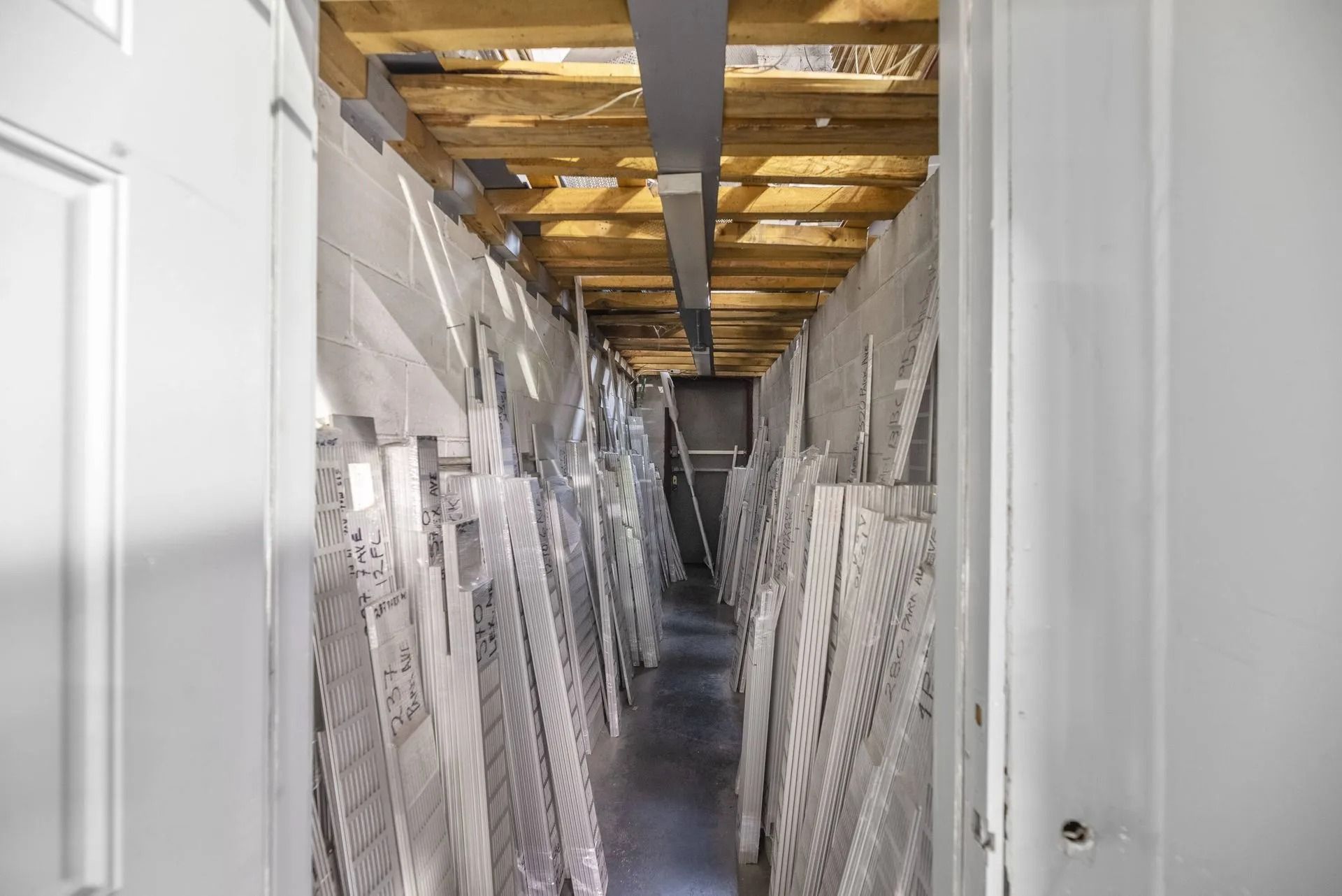 Narrow storage hallway with stacked white doors or panels leaning along both sides under exposed ceiling joists