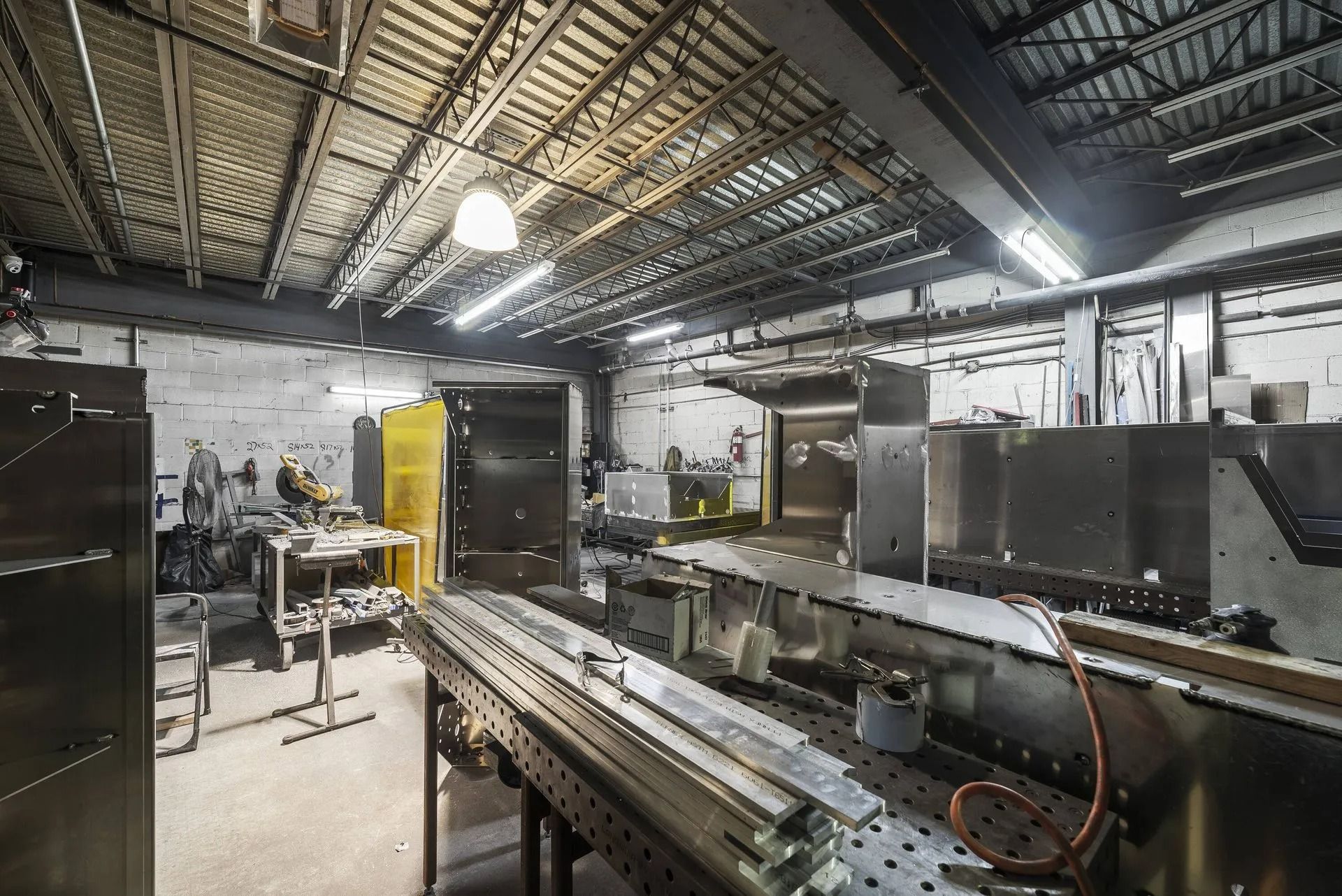 Industrial workshop with machinery, metal workbenches, and overhead lighting in a large factory space