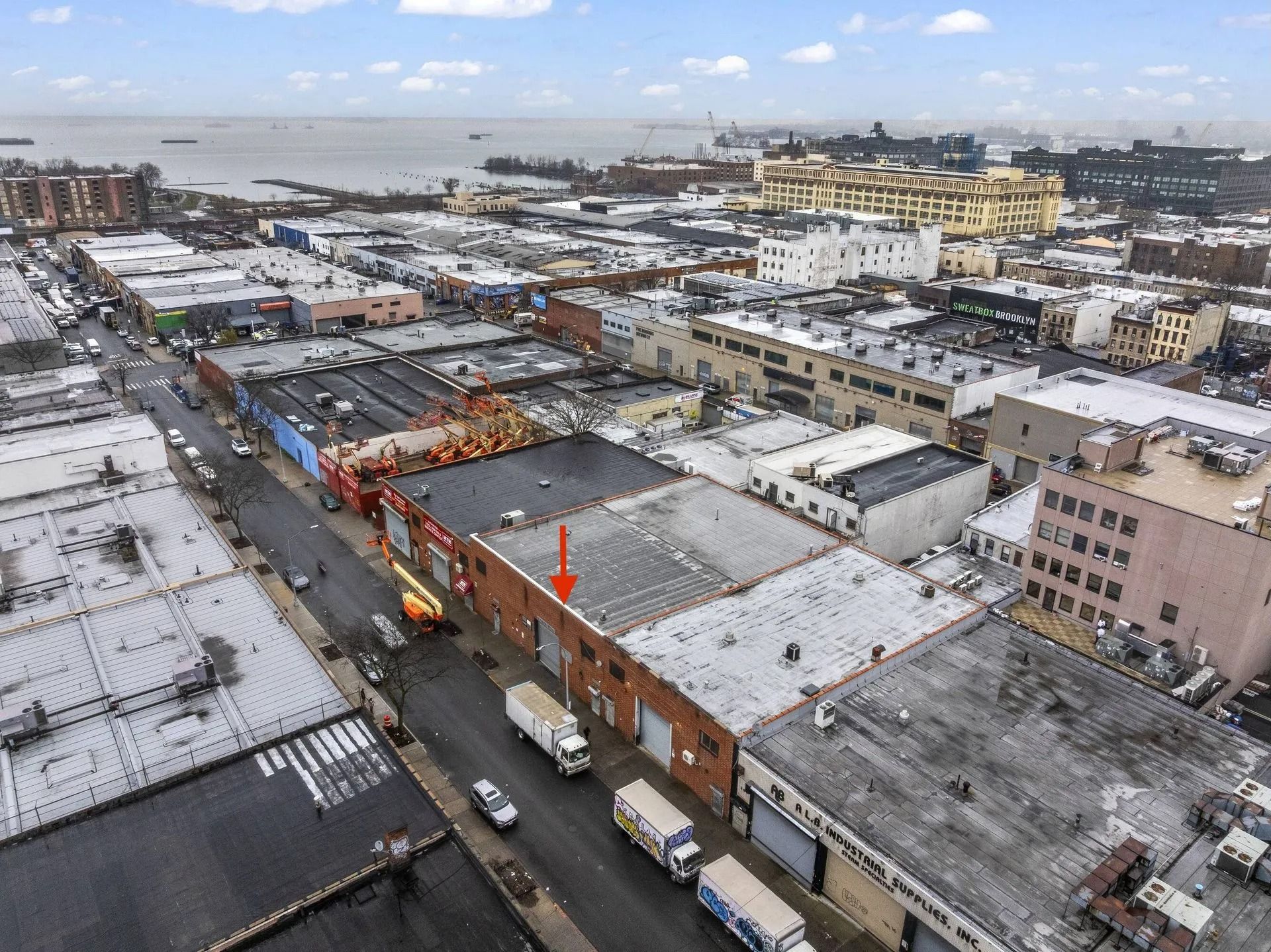 Snowy aerial view of a city block with parked trucks, brick buildings, and a busy street