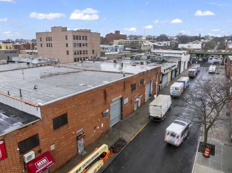 Overhead view of a wet city street beside brick warehouses and parked trucks on a cloudy day