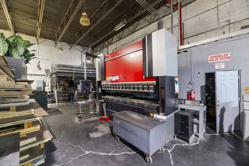 Industrial workshop with a large red-and-gray machine beside stacks of boards and tools.