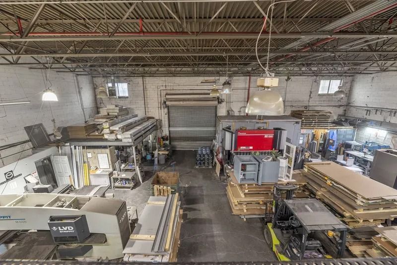 Wide shot of a woodworking factory with stacks of lumber, machinery, and a few workers inside a warehouse