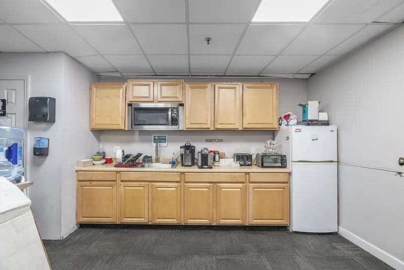 Office break room with kitchenette, white fridge, wood cabinets, and countertop appliances