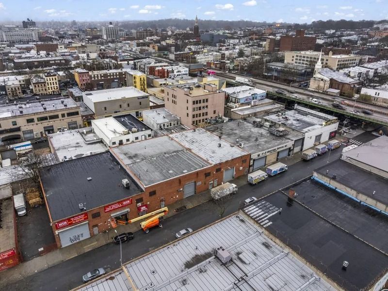 Aerial view of an urban neighborhood with low-rise buildings, rooftops, and snowy streets under a cloudy sky